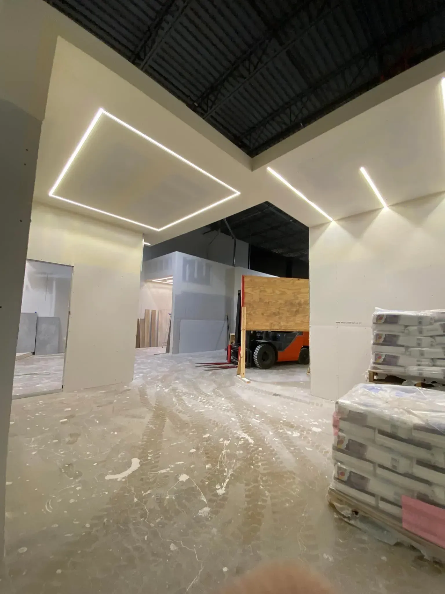 Warehouse interior with stacked materials, plastic-wrapped pallets, and bright geometric ceiling lights