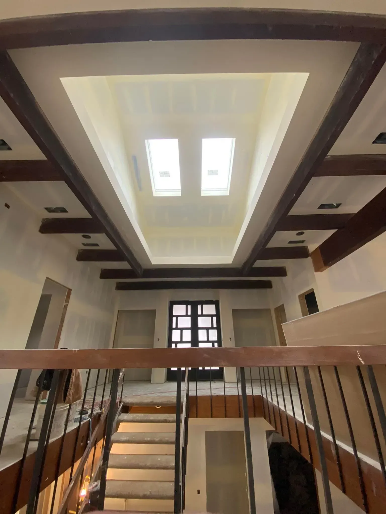 Staircase with wooden railing and dark ceiling beams beneath a skylight in a bright interior hall