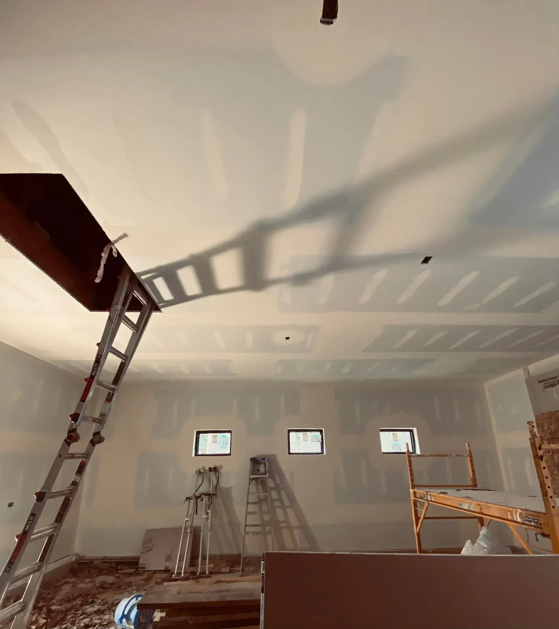 Interior room under renovation with ladders, scaffolding, and shadowed ceiling work.