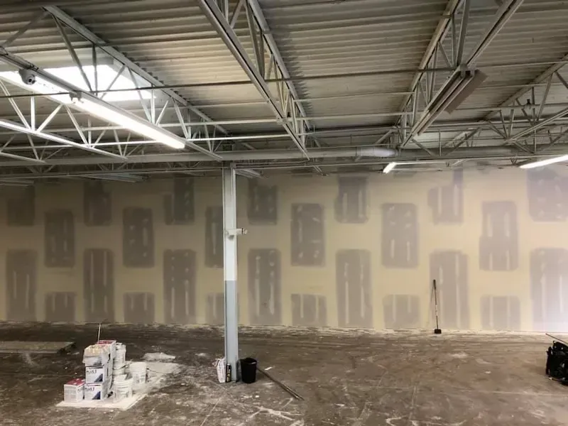 Empty industrial room with unfinished drywall, exposed ceiling beams, and construction materials on the floor