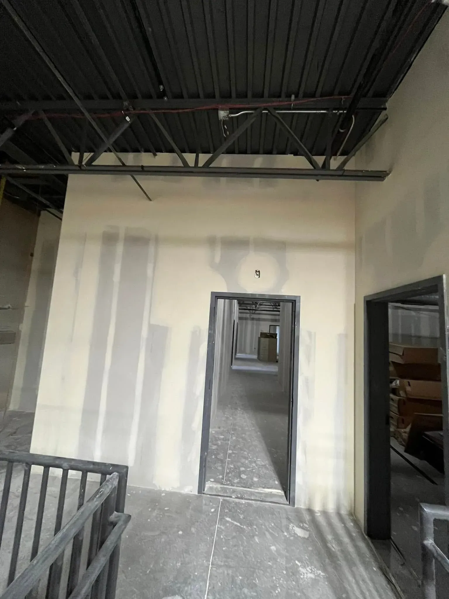 Interior hallway under construction with unfinished drywall, exposed ceiling, and doorways leading deeper inside.