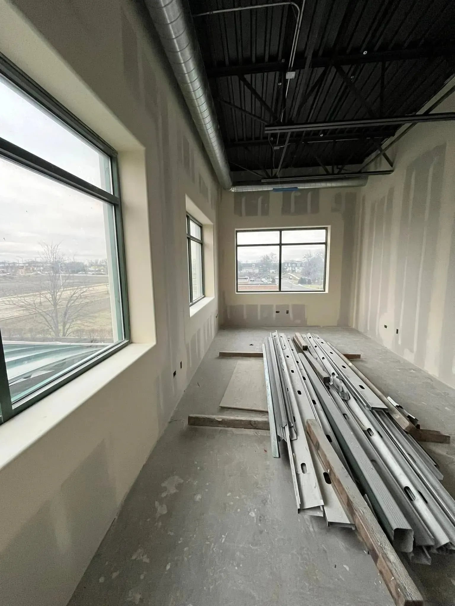Unfinished room with exposed ceiling, long windows, and stacked white construction materials on the floor.