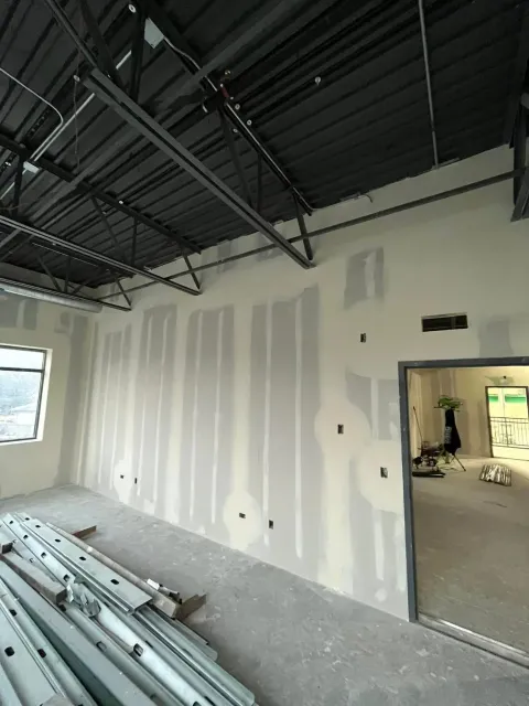 Interior of a construction site with drywall, exposed ceiling beams, and stacked metal studs.