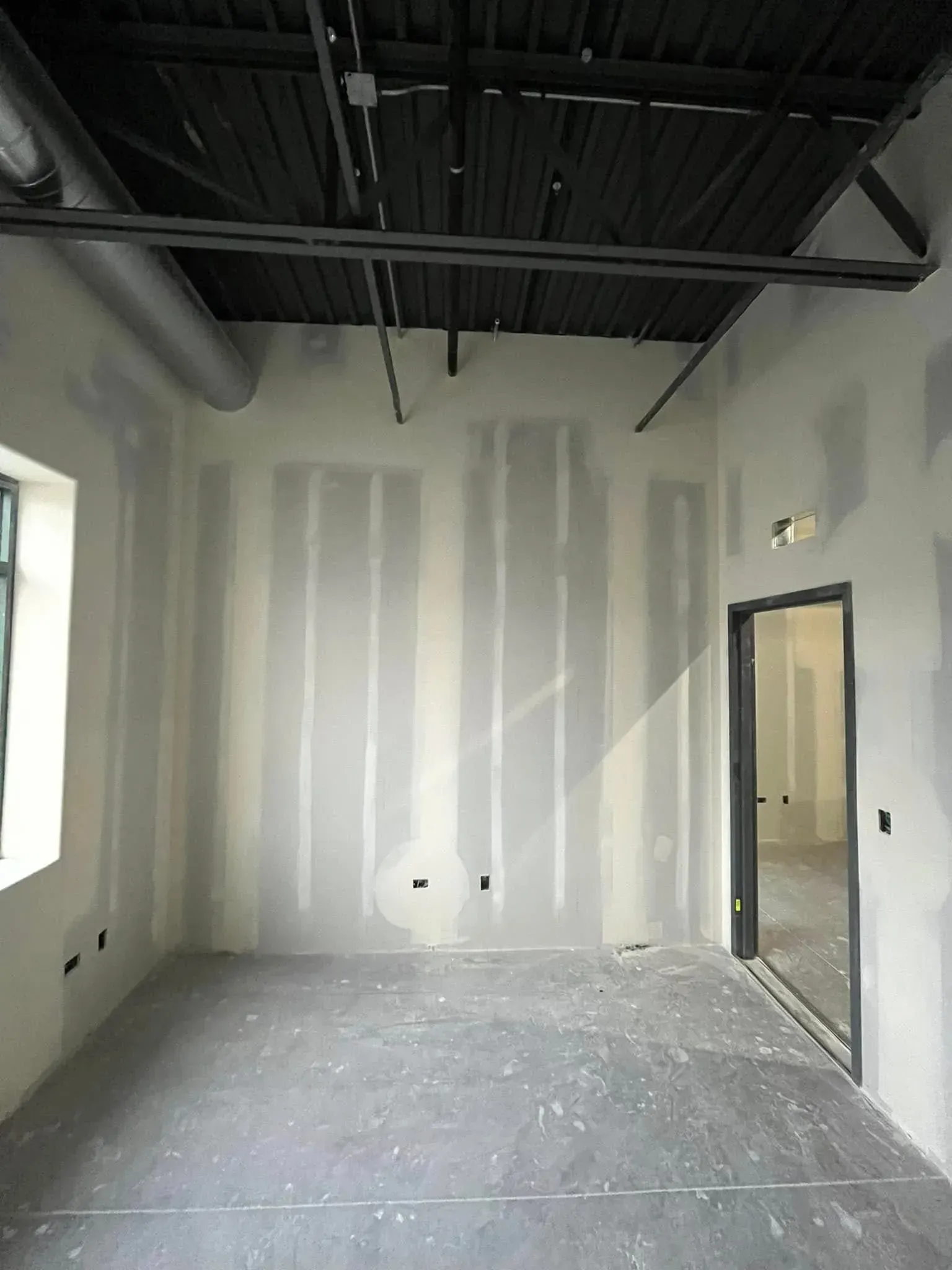 Empty unfinished room with drywall, exposed black ceiling, and a doorway on the right.