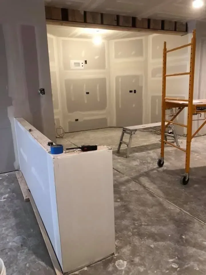 Renovation site with drywall, scaffolding, and a partially built white half-wall indoors
