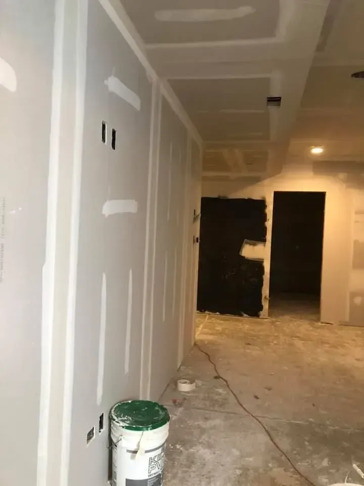 Narrow hallway under renovation with drywall, paint bucket, and unfinished walls and floor