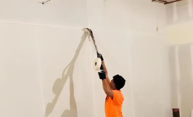 Worker in orange shirt using a drill to install a ceiling fixture in a room