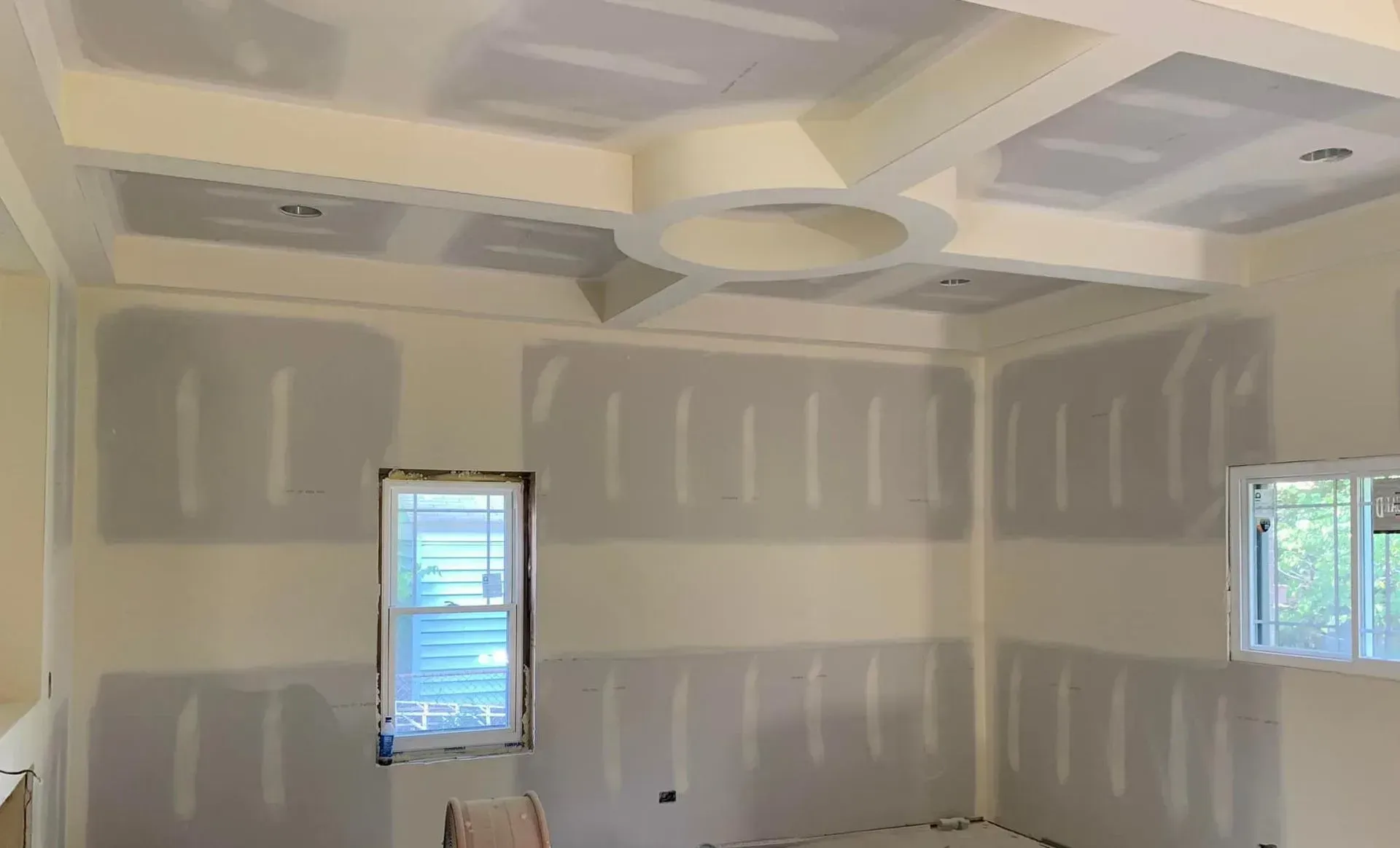 Unfinished room with drywall, taped seams, recessed ceiling detail, and two windows with blinds.