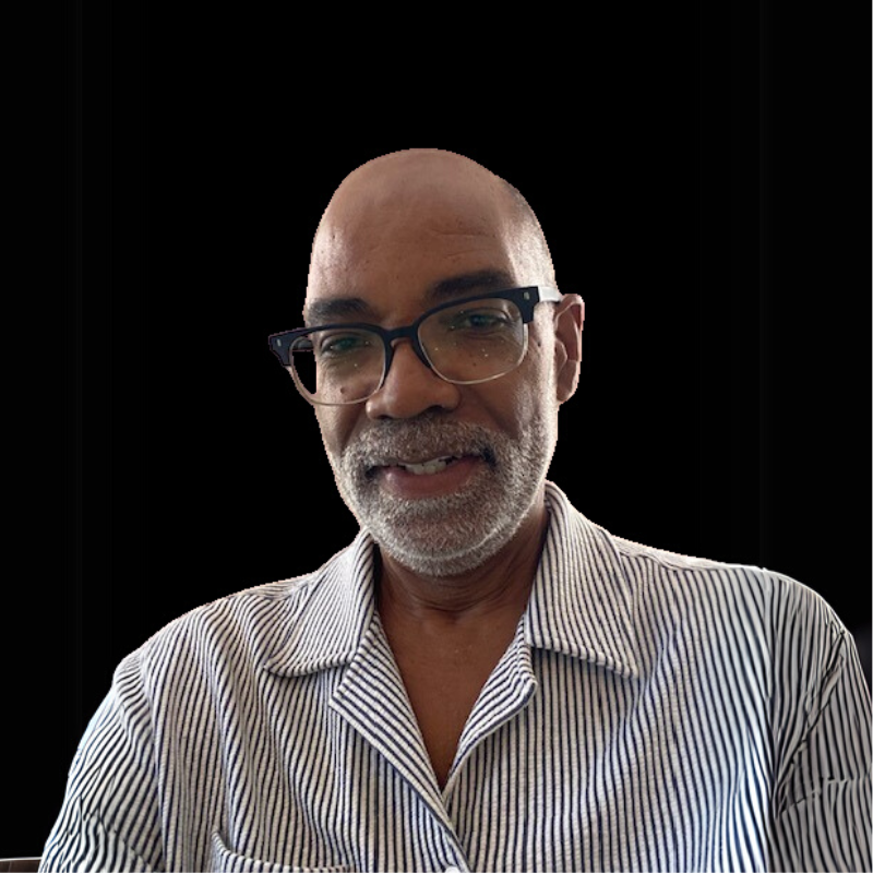 Trey the Executive Director. A man with a gray beard and glasses, wearing a blue and white striped shirt, smiling against a black background.
