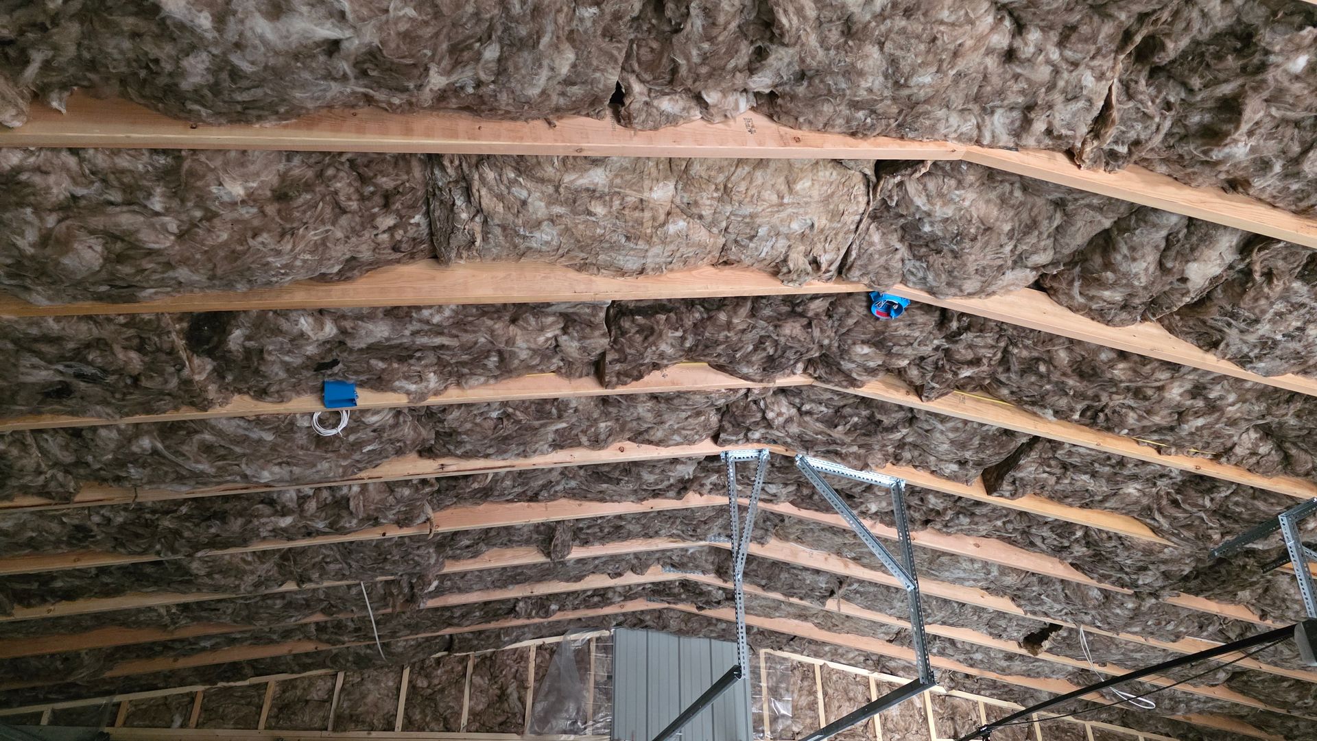 Insulation installed between wooden rafters in a building's ceiling, with electrical boxes visible.