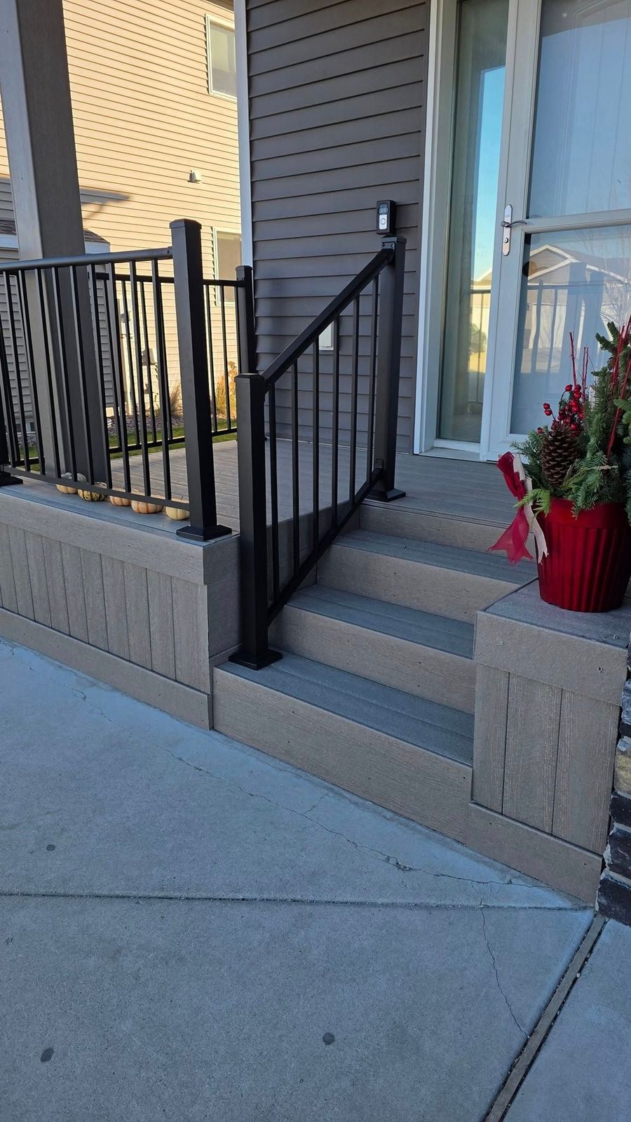 Exterior view of a home entrance with concrete stairs, black railing, and decorative flower pot.