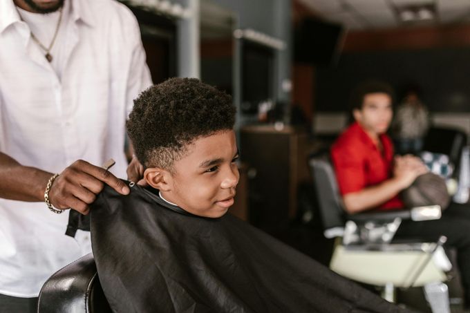 A stylist with black gloves washes a client's wet, dark hair in a salon sink.