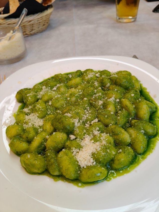 Piatto di gnocchi conditi con pesto verde e ricoperti di formaggio grattugiato.