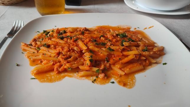 Piatto di penne al pomodoro con erbe aromatiche su un tavolo bianco di ristorante