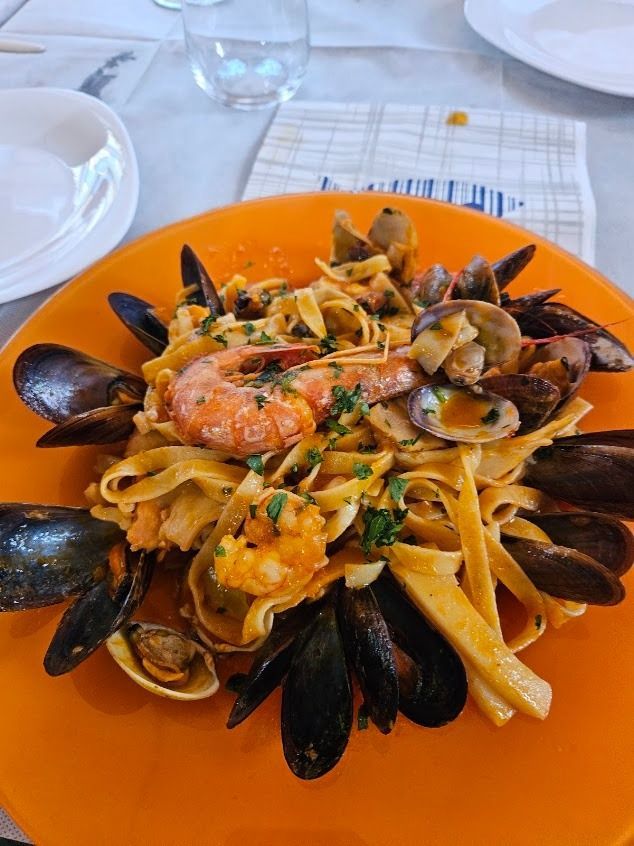 Pasta ai frutti di mare con cozze, gamberi ed erbe aromatiche, servita su un piatto arancione