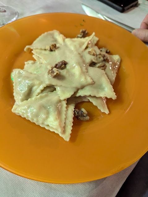 Ravioli su un piatto arancione, guarniti con frutta secca tritata o salsa, tenuti in mano