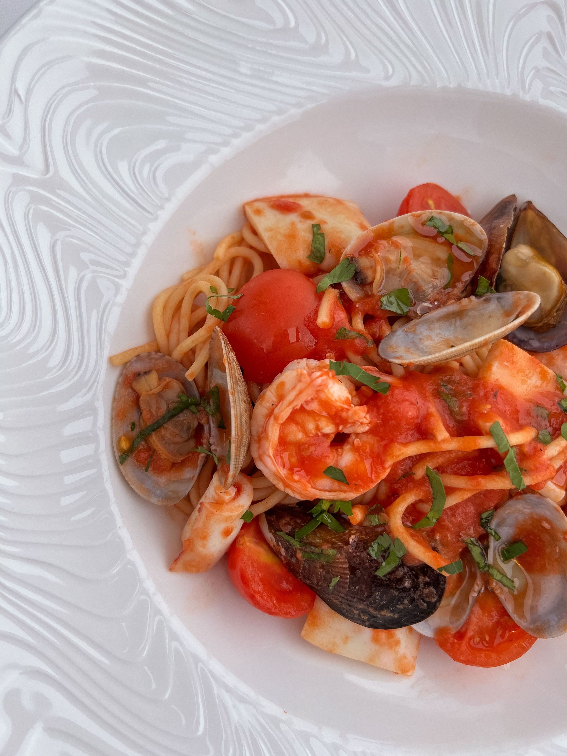 Pasta ai frutti di mare al sugo di pomodoro con vongole, gamberi e basilico, servita su un piatto bianco