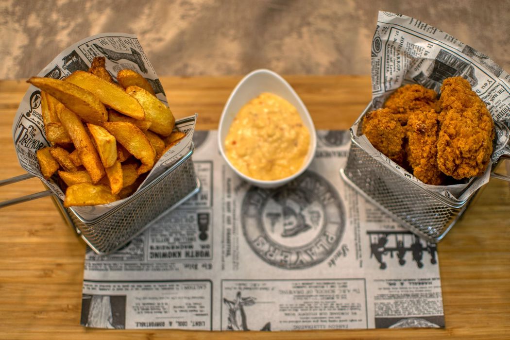 Cestino di patatine fritte e pollo fritto con una ciotola di salsa da intingere su un tavolo di legno rivestito di carta di giornale