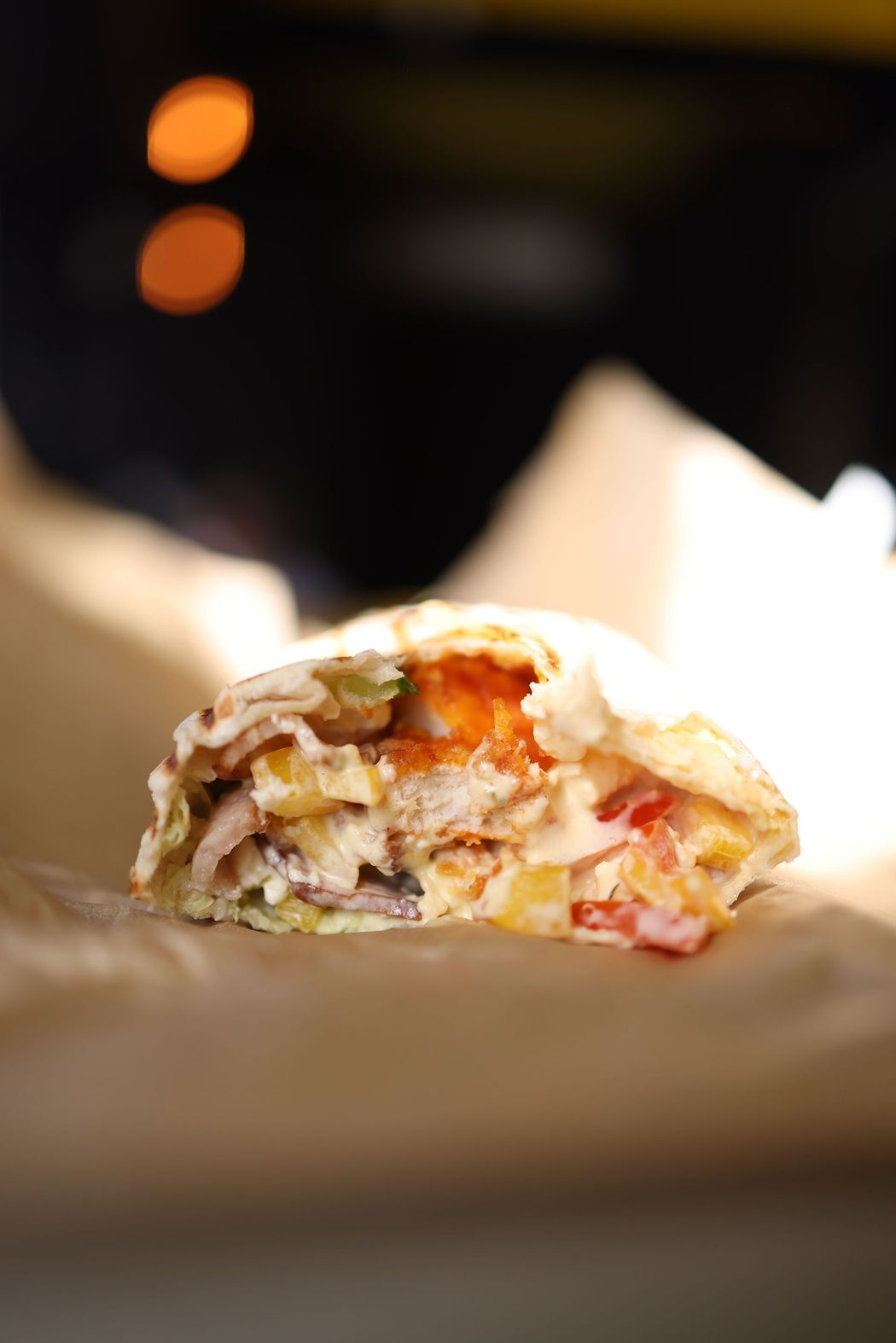 Primo piano di un panino o wrap morsicato, su carta da forno, con uno sfondo scuro sfocato