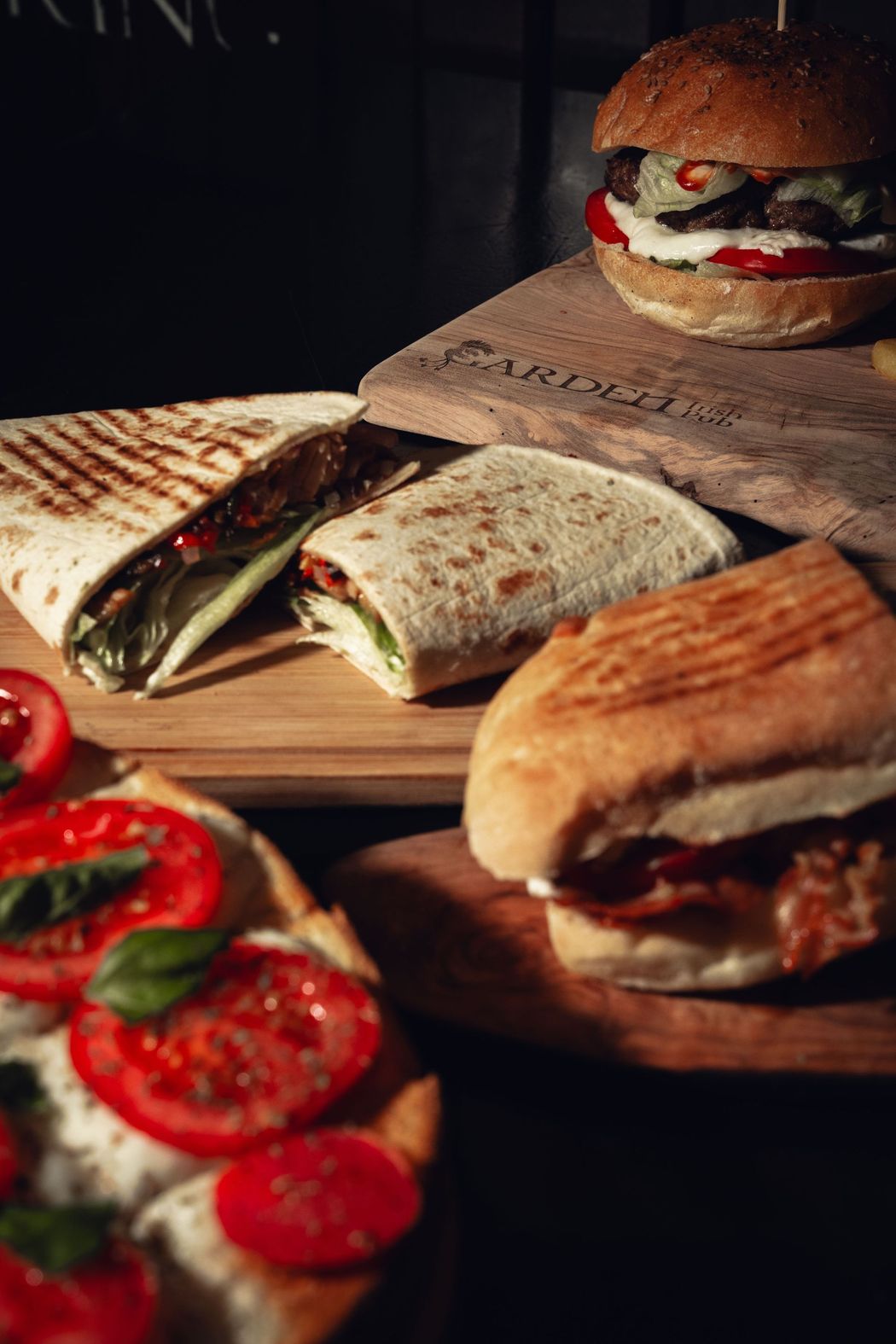 Panini e wrap assortiti su taglieri di legno, con pomodori a fette in primo piano.