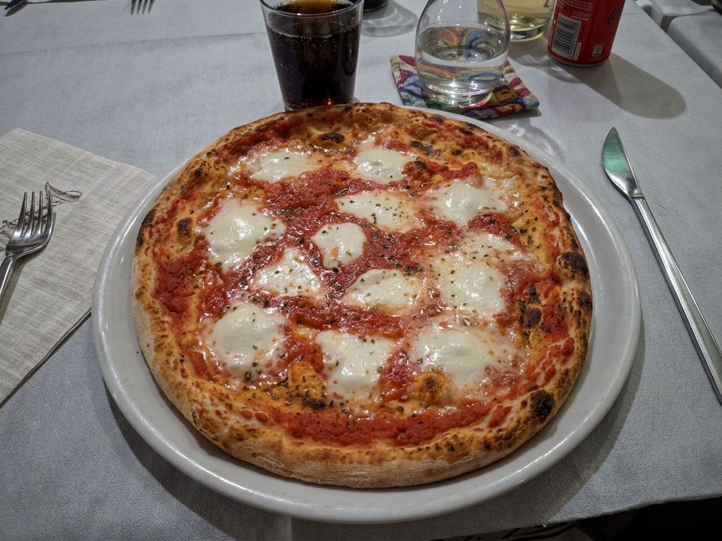 Pizza Margherita su un piatto, su un tavolo di ristorante, con una bevanda e le posate