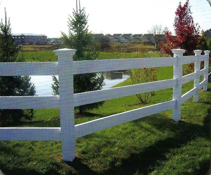 White three-rail fence in a grassy yard, with trees and a pond visible in the background.
