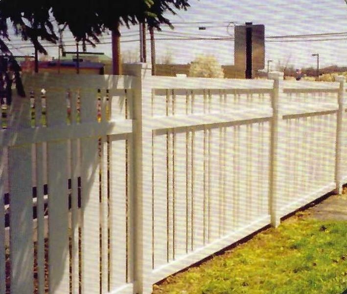 White vinyl fence in a grassy area, with trees and buildings in the background.
