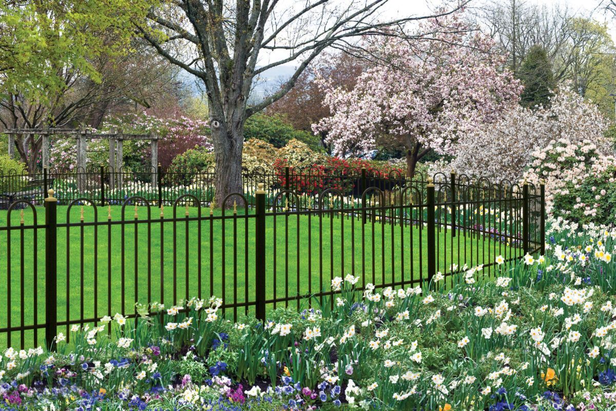 Flower-filled park garden with black fence, blooming trees, and green lawn in spring