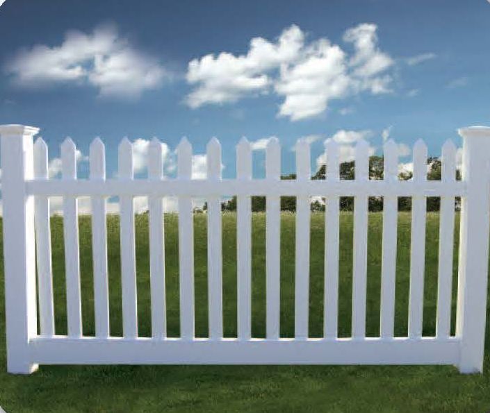 White picket fence in front of a green field with a blue sky and clouds.