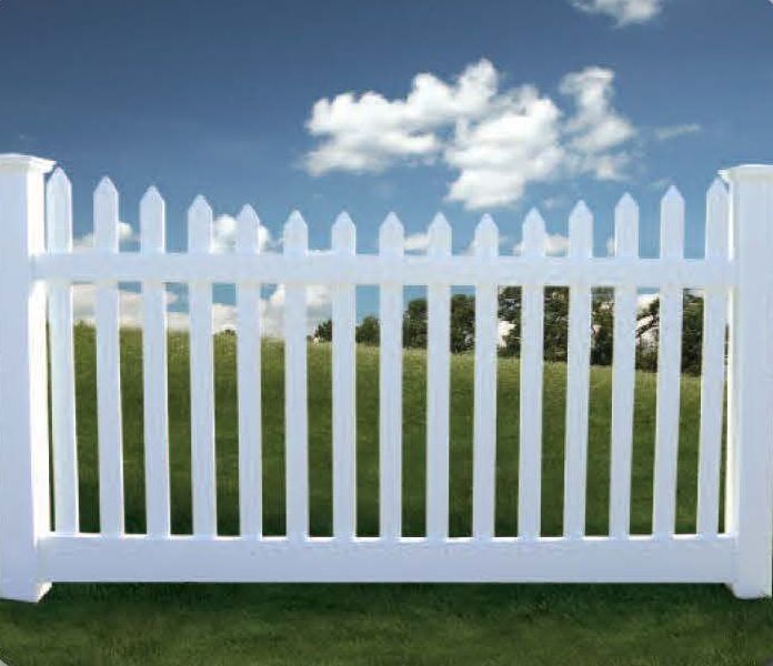 White picket fence in front of green grass and trees with a blue sky and clouds.