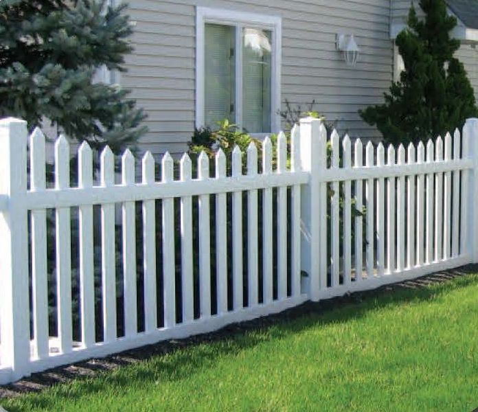 White picket fence bordering a green lawn in front of a house with window and trees.