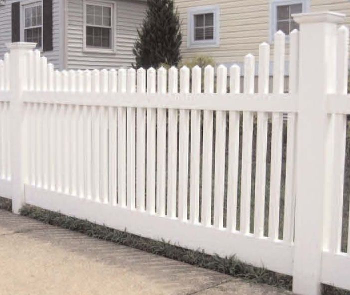 White picket fence in front of a house with a light-colored exterior and small front lawn.