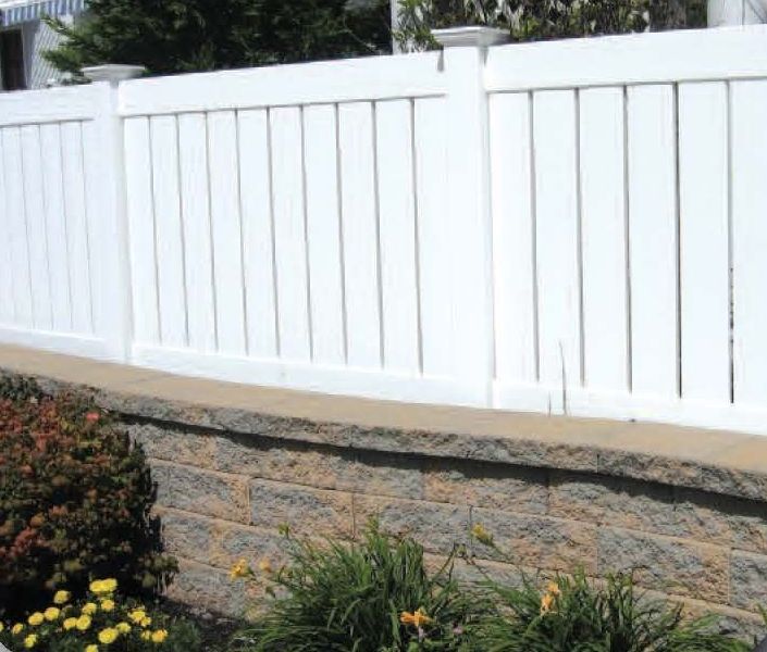 White vinyl fence atop a retaining wall with greenery in front.