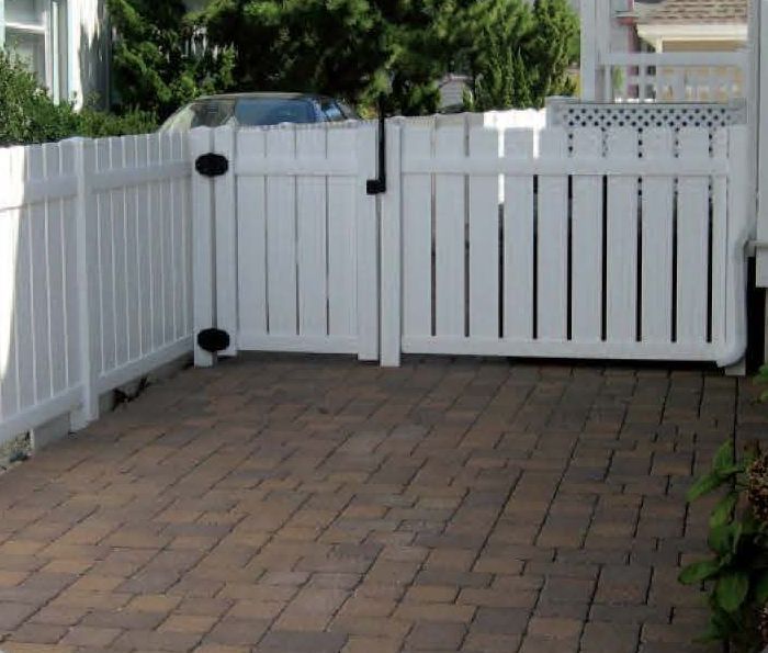 White picket fence with a gate on a brick patio. A car is visible behind the fence.