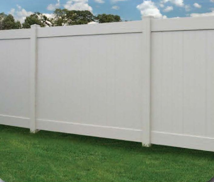 White vinyl privacy fence in a grassy yard against a blue sky.