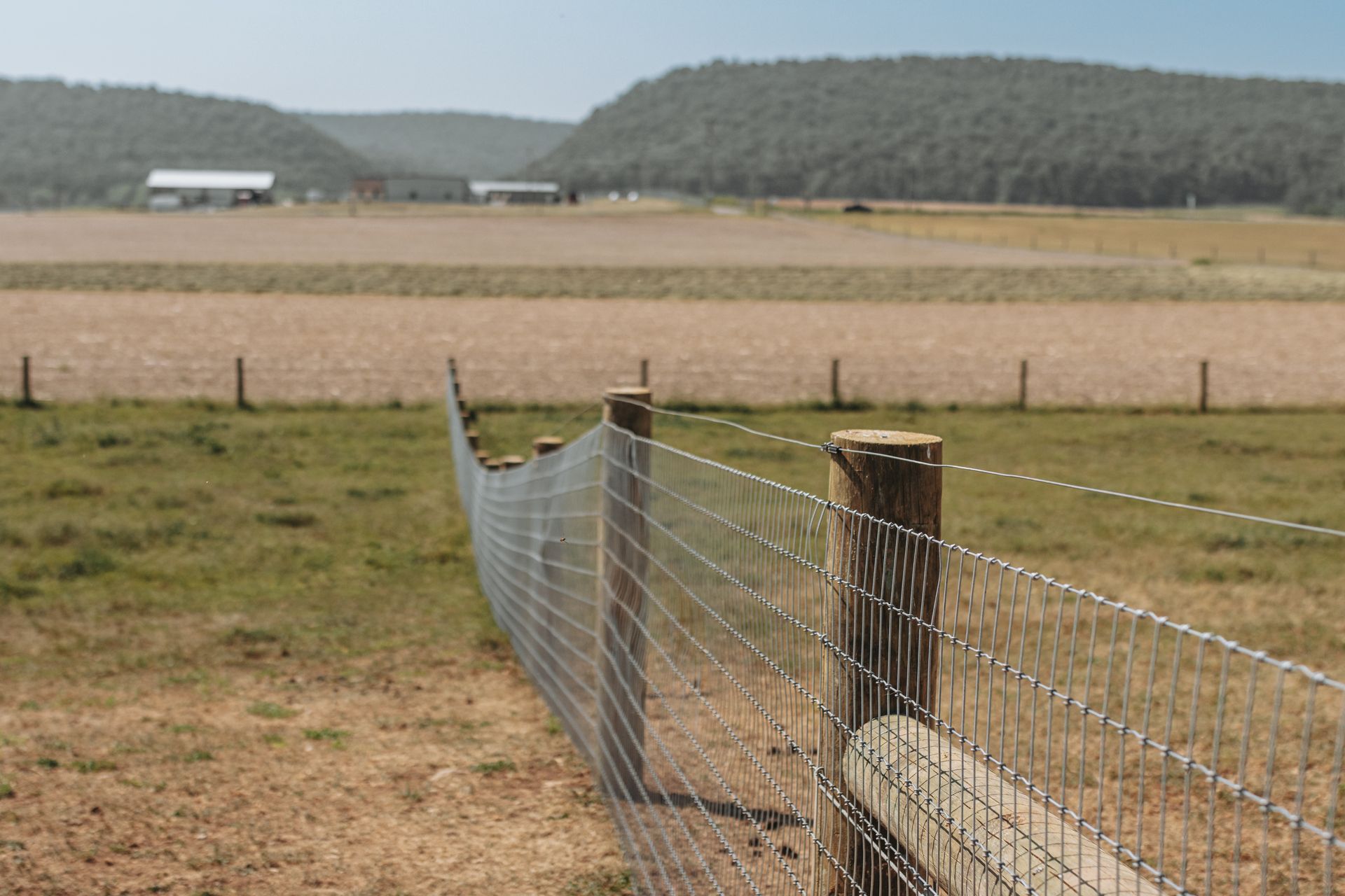 Fence in a field with farmland and hills in the distance.