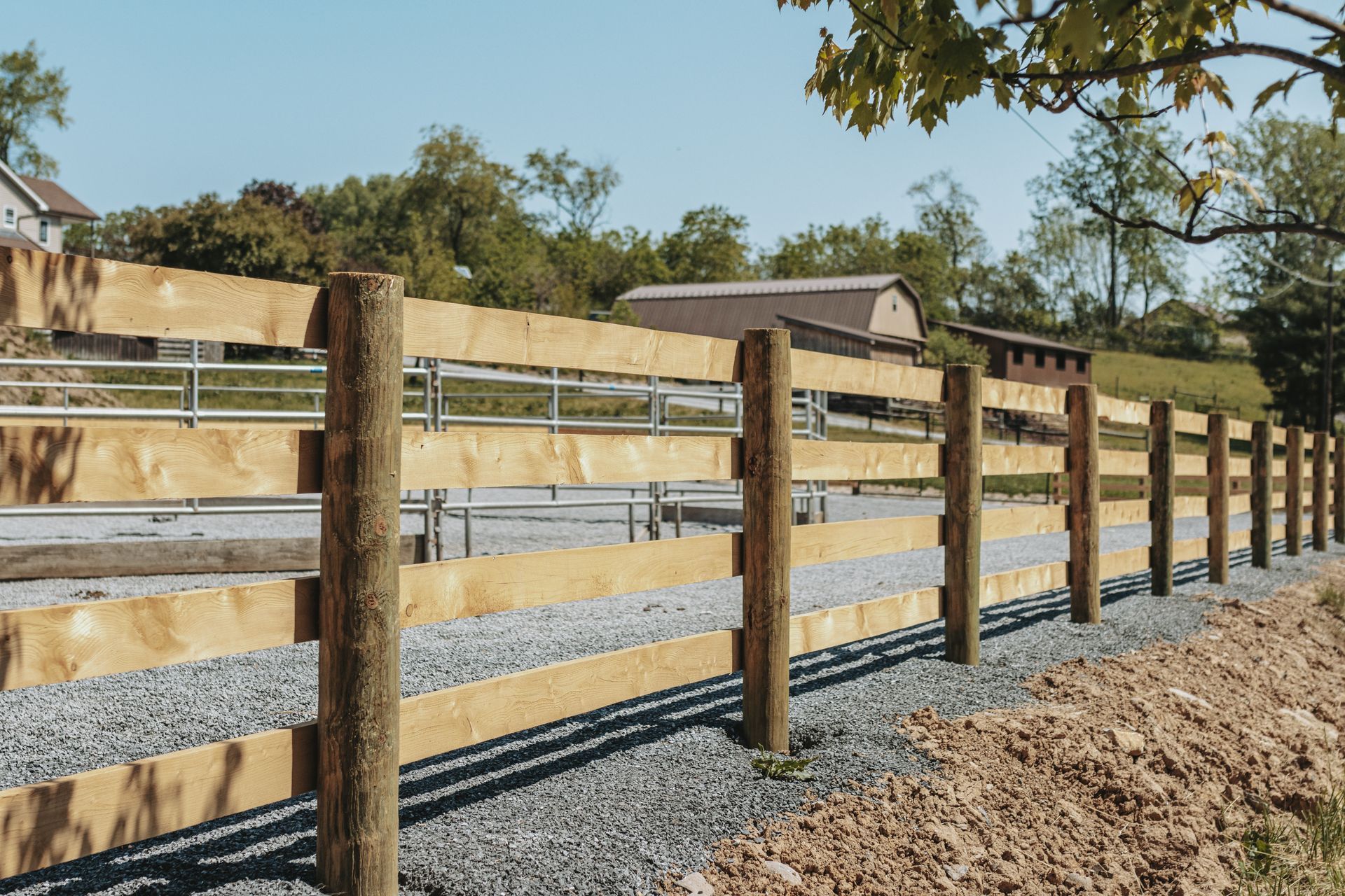 Wooden fence bordering a gravel path and trees, with a metal gate visible further in.