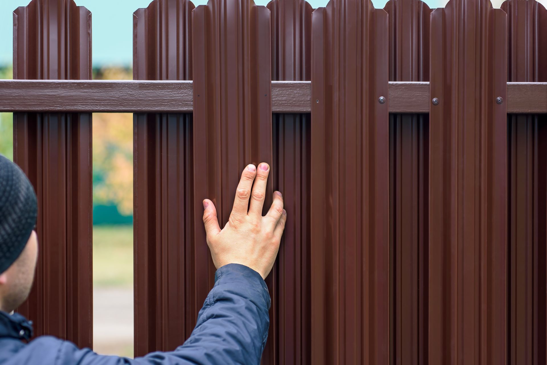 Hand touching a brown wooden fence with a horizontal metal bar in Central PA during winter.