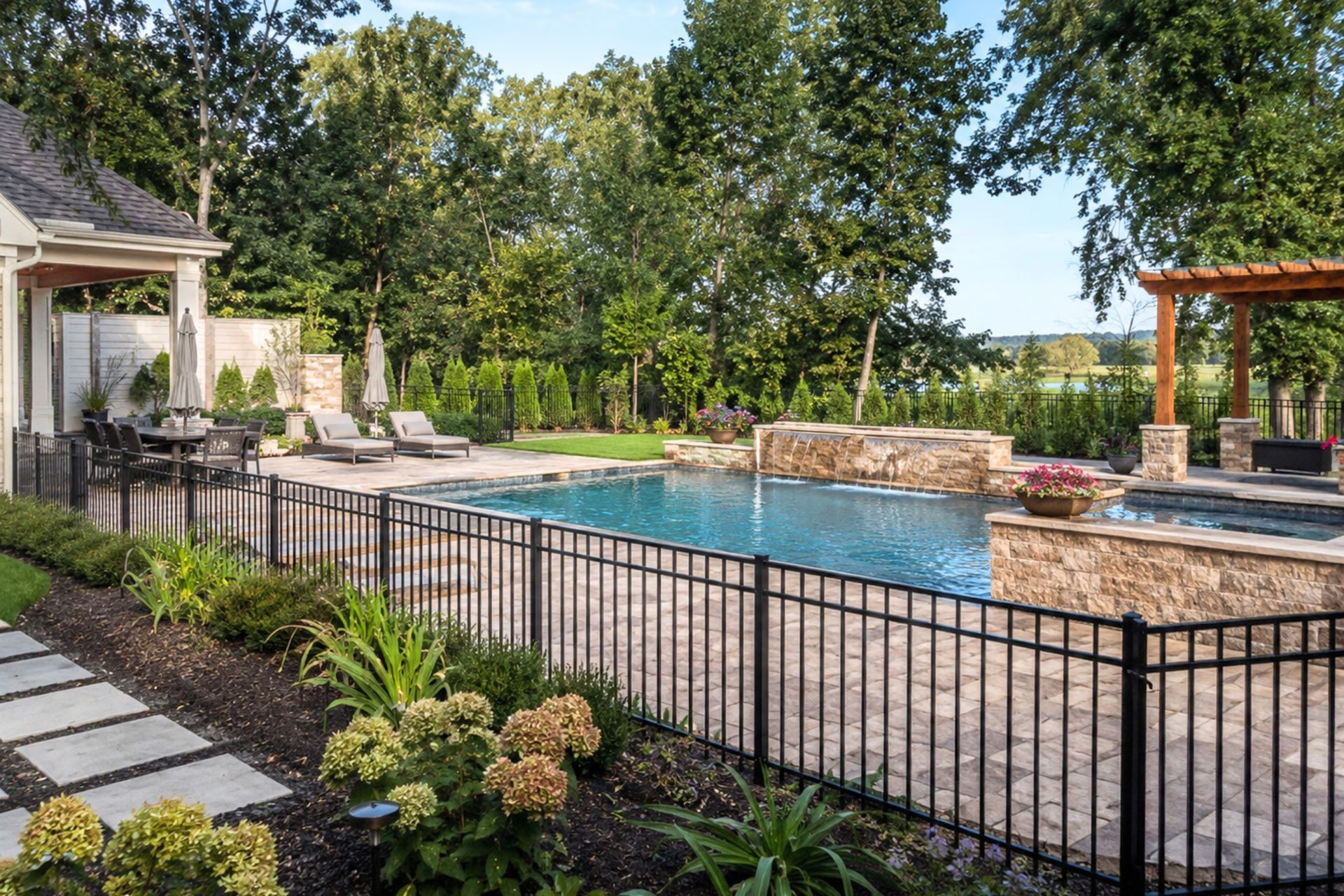 Backyard with a fenced swimming pool, patio seating, and lush landscaping under trees in Central PA