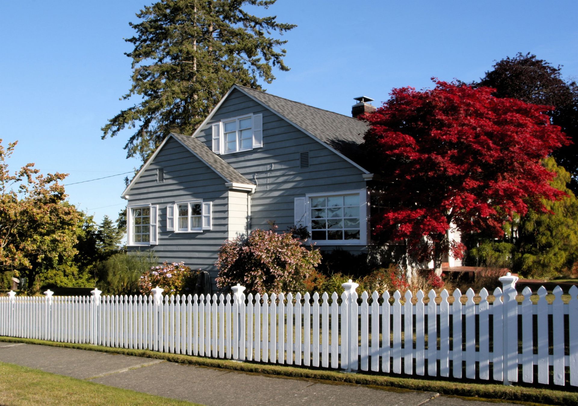 Gray house with a white picket fence and red-leaved tree in Central PA under a clear blue sky.