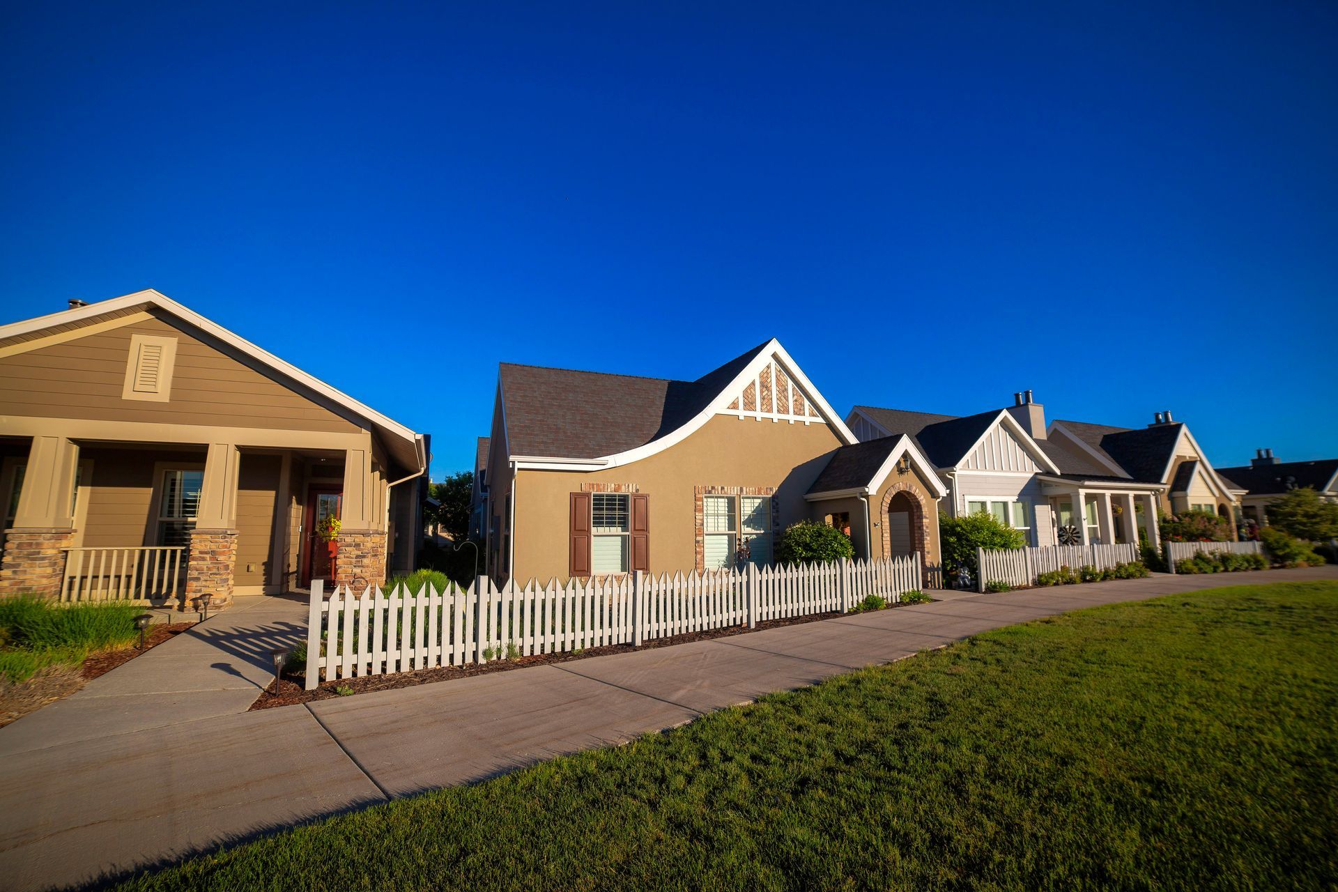 Row of tan suburban houses with white picket fences under a clear blue sky