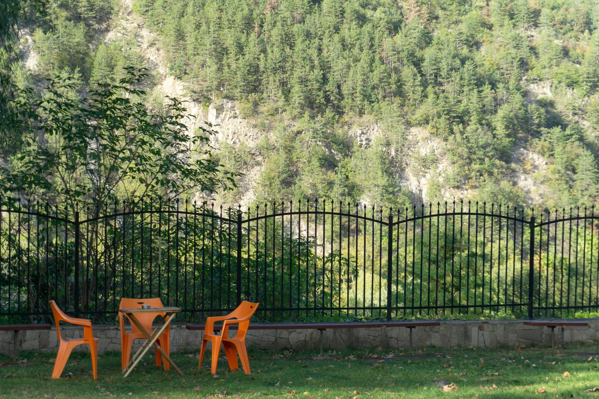 Orange chairs and a table on a grassy lawn beside a black fence in State College