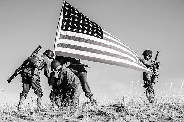 Soldiers raising American flag on a hillside, black and white.