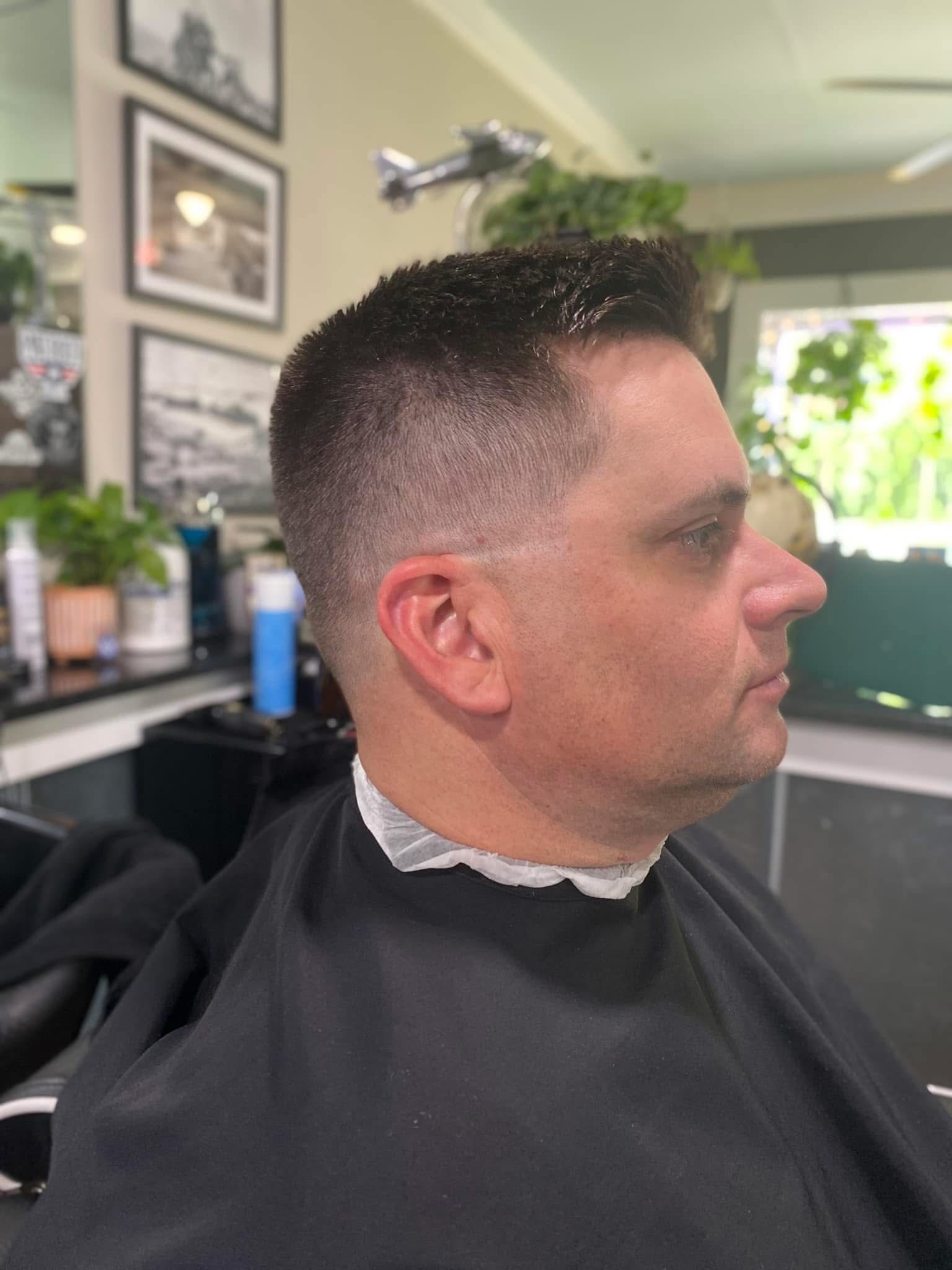 Man in barber chair with a tapered haircut, side view. Dark hair, black cape.