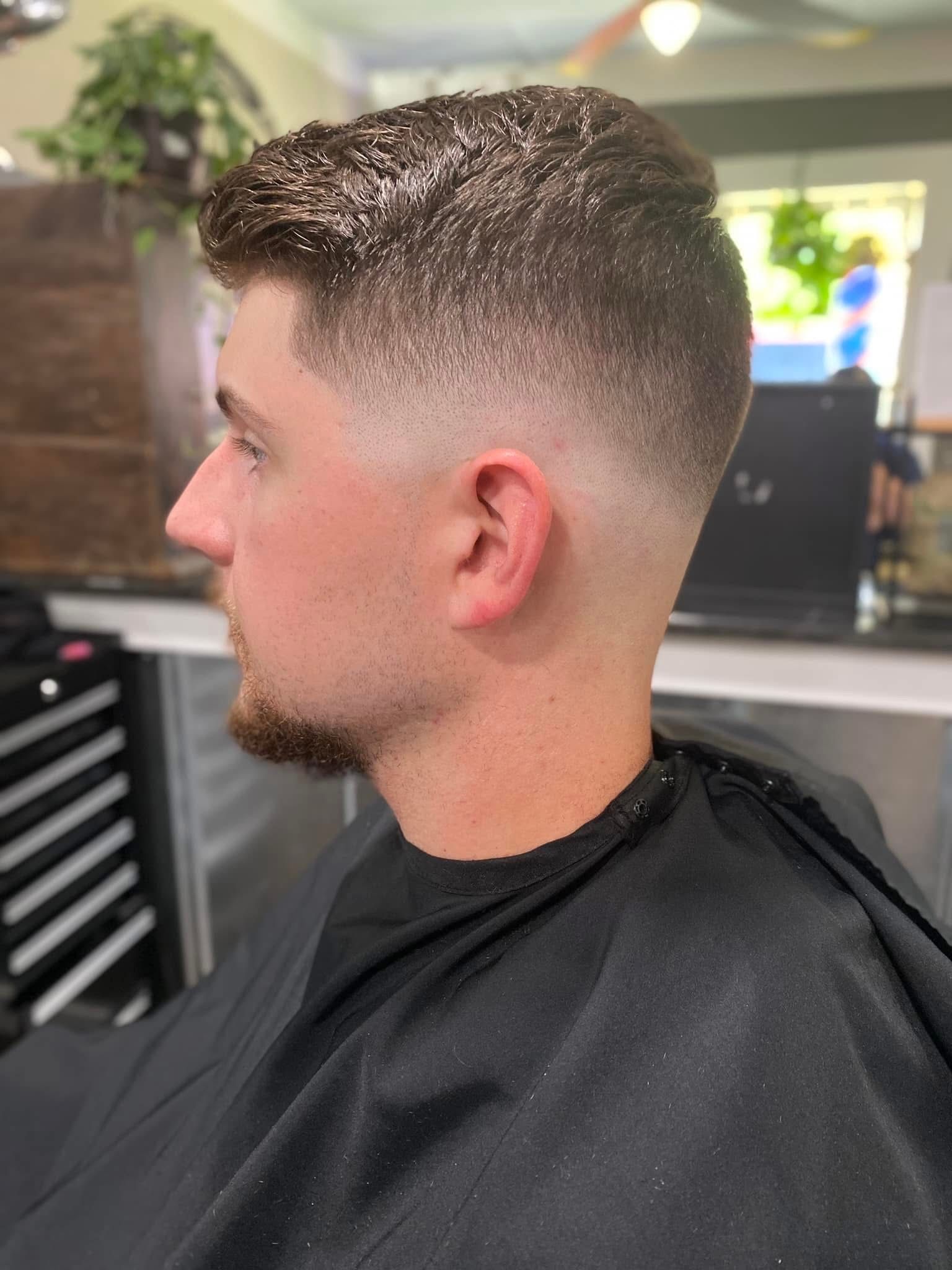 Man with a faded haircut, dark hair on top, sitting in a barber chair.