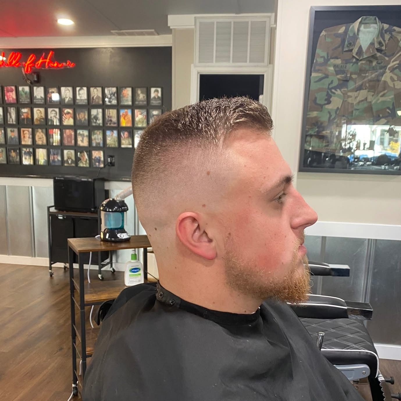 Man with a faded haircut at a barbershop. He has a beard and is wearing a black cape.