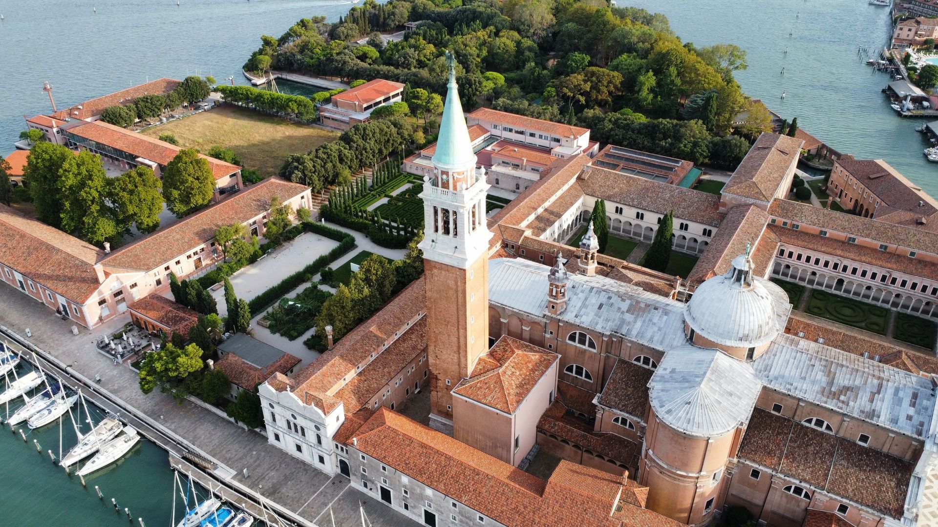 Aerial view of Venice’s historic island with red-roofed buildings, bell tower, and domes beside the lagoon.