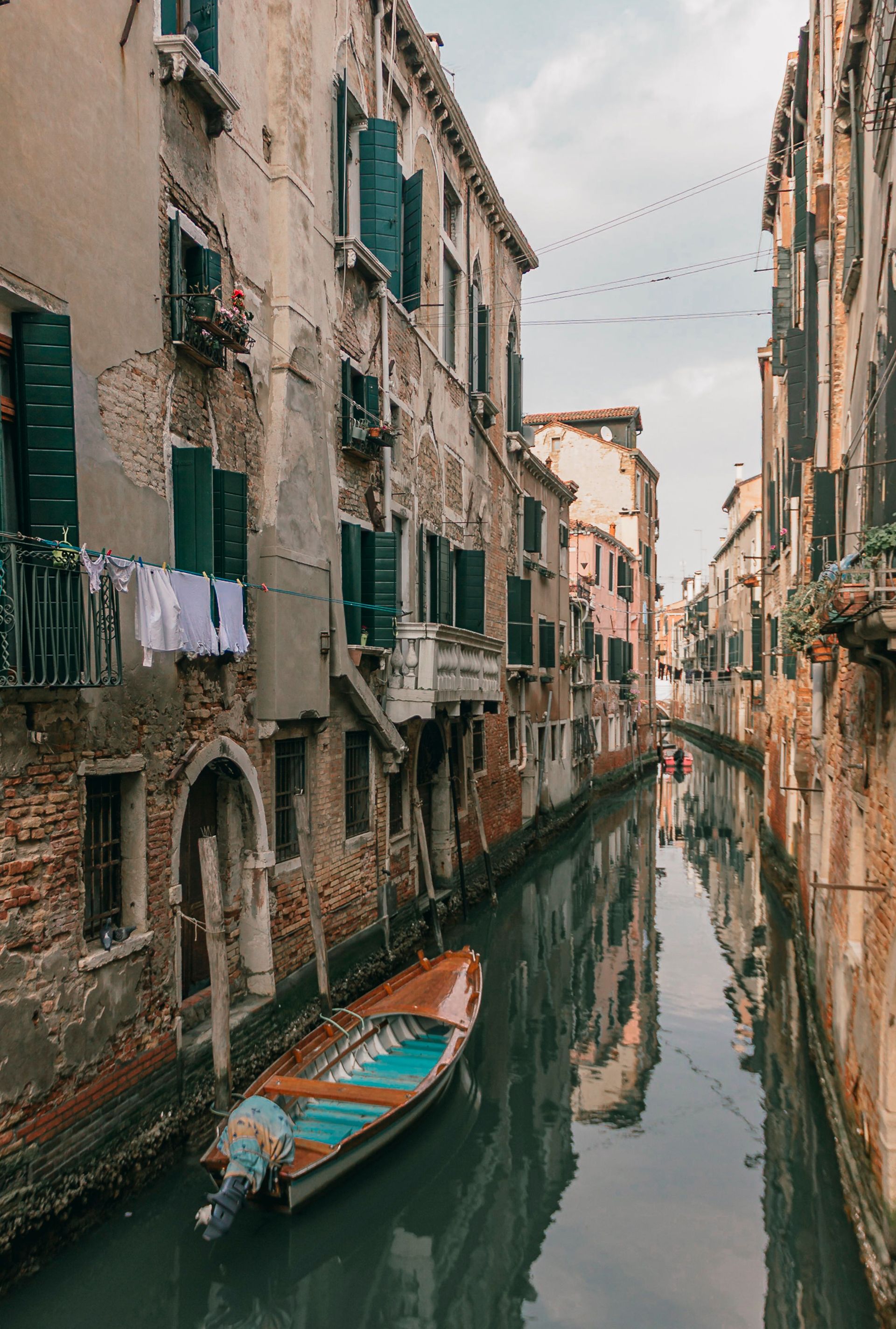 Narrow Venice canal lined with weathered buildings and a small turquoise boat floating on calm water