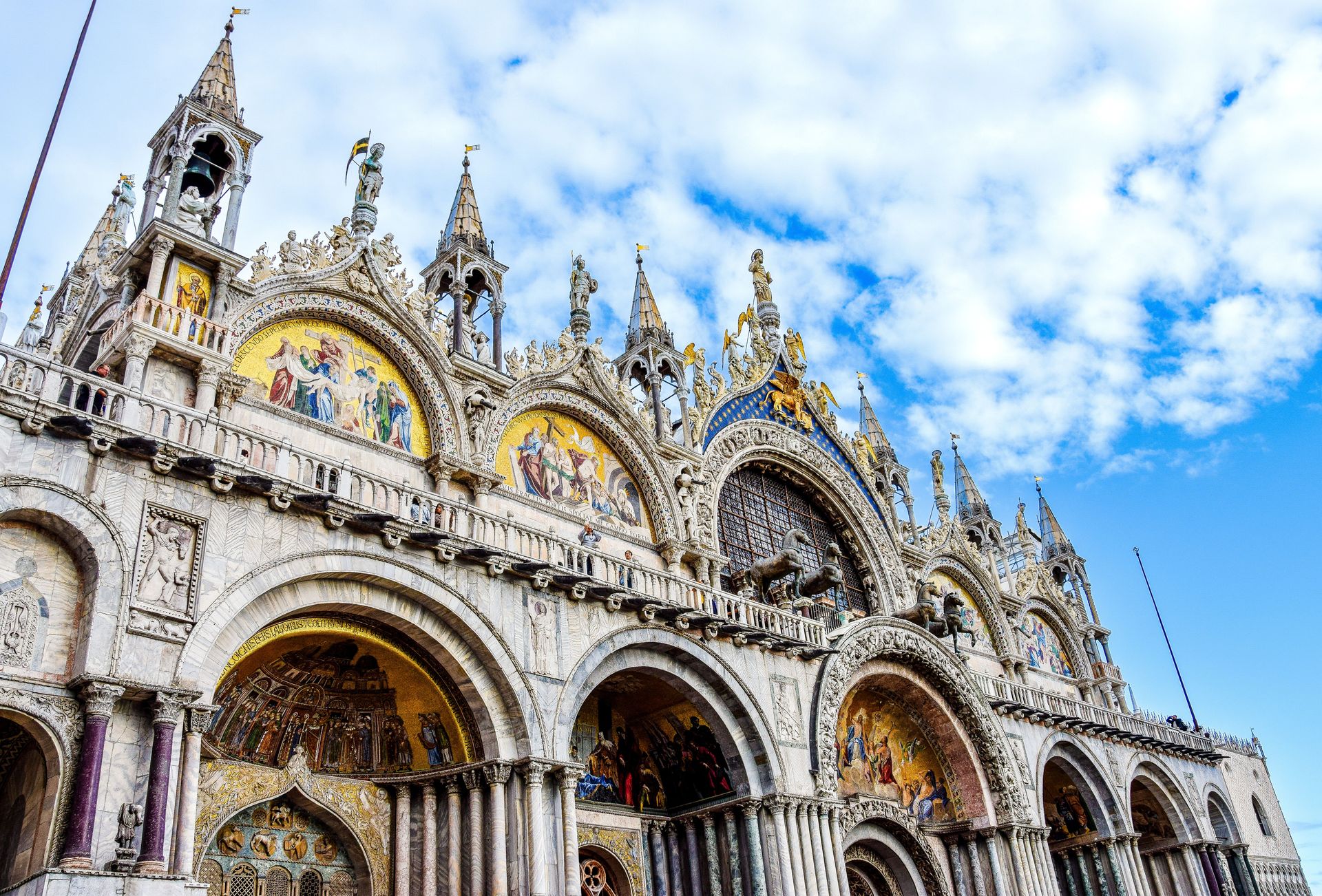 Ornate cathedral facade with mosaics and arches against a blue, cloudy sky