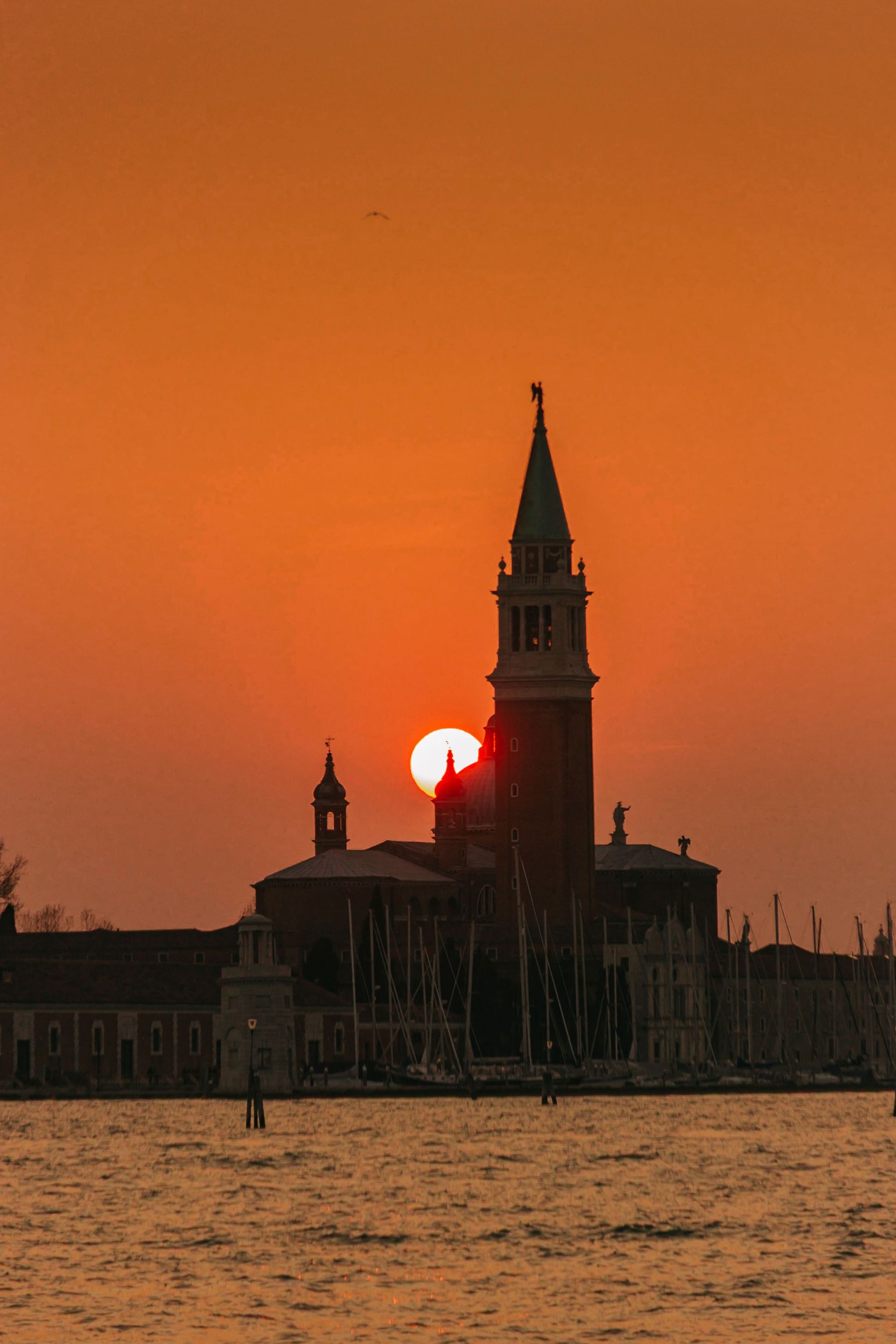 Sunset behind a tall church tower and bell tower silhouetted over water